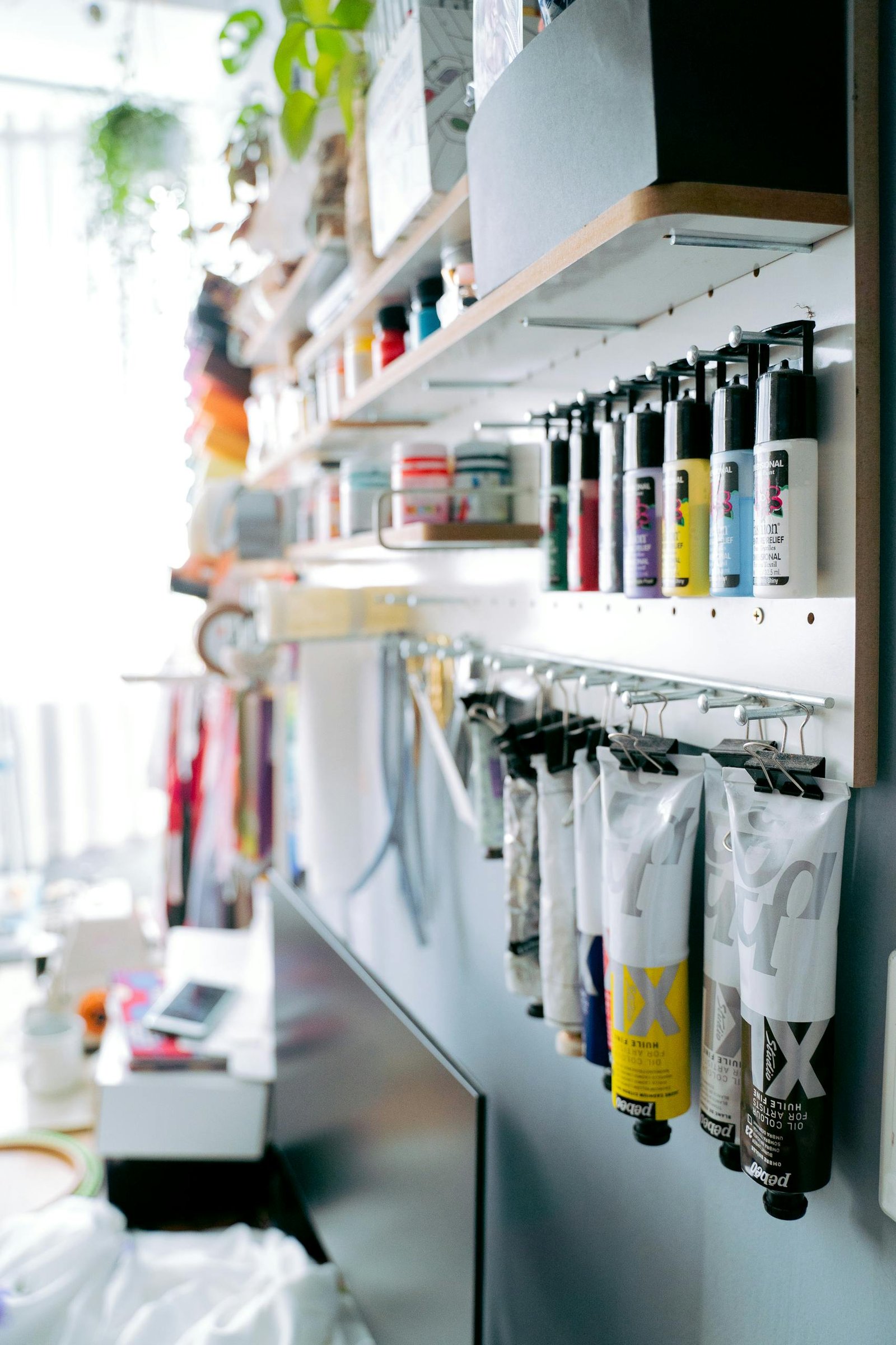 A well-organized art studio featuring paint tubes and supplies on wooden shelves.